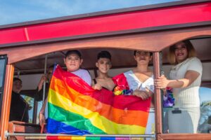 Four people on a trolley holding a Pride flag